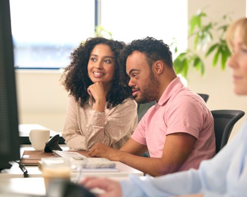 woman-working-in-office-based-business-training-man-with-down-syndrome-using-computer
